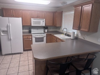 Kitchen featuring white appliances, a sink, a peninsula, a breakfast bar, and light tile patterned floors