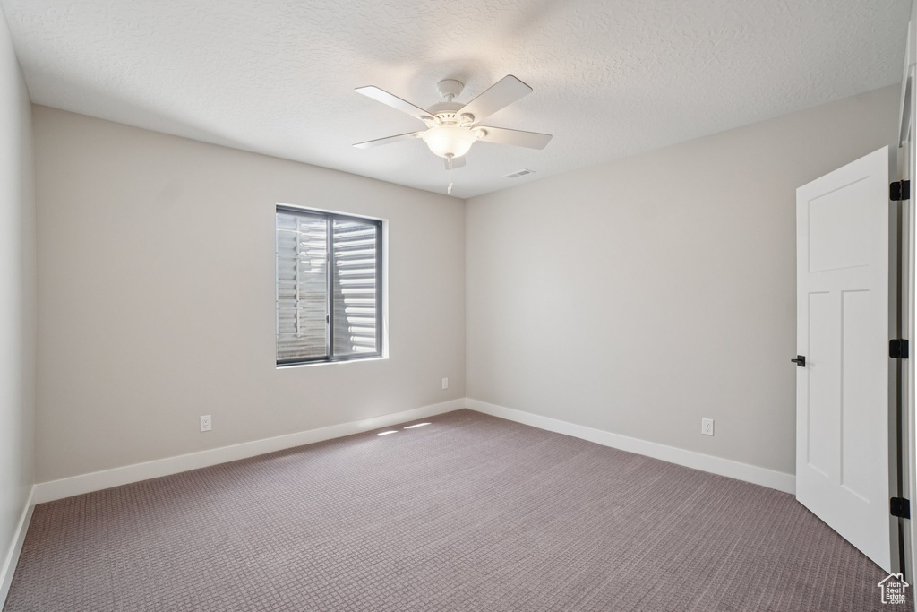 Empty room featuring carpet flooring, baseboards, ceiling fan, and a textured ceiling