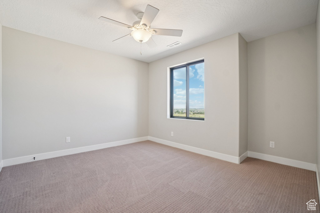 Empty room featuring light carpet, a ceiling fan, baseboards, and a textured ceiling