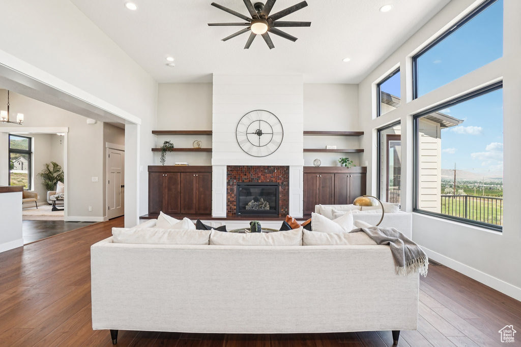 Living room with healthy amount of natural light, ceiling fan, a fireplace, dark wood-type flooring, and recessed lighting