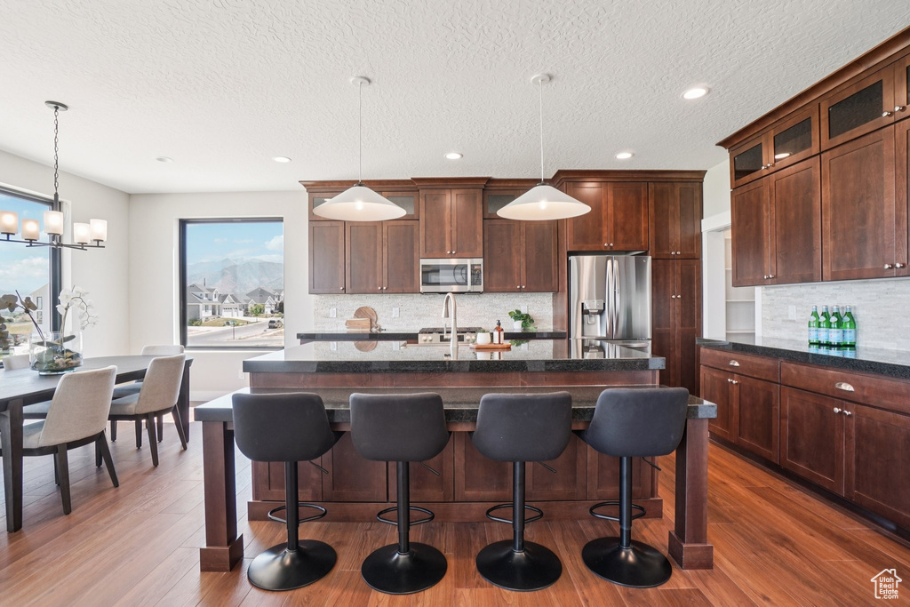 Kitchen featuring appliances with stainless steel finishes, tasteful backsplash, a center island with sink, glass insert cabinets, and a kitchen bar