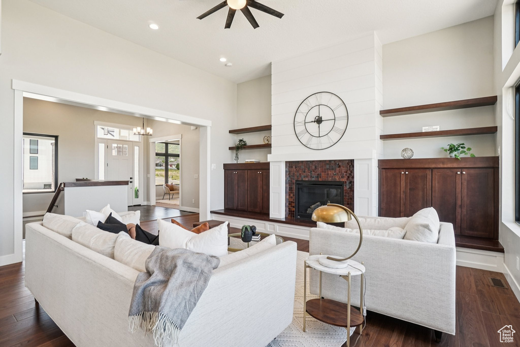 Living area featuring a ceiling fan, a glass covered fireplace, dark wood-style flooring, a chandelier, and recessed lighting