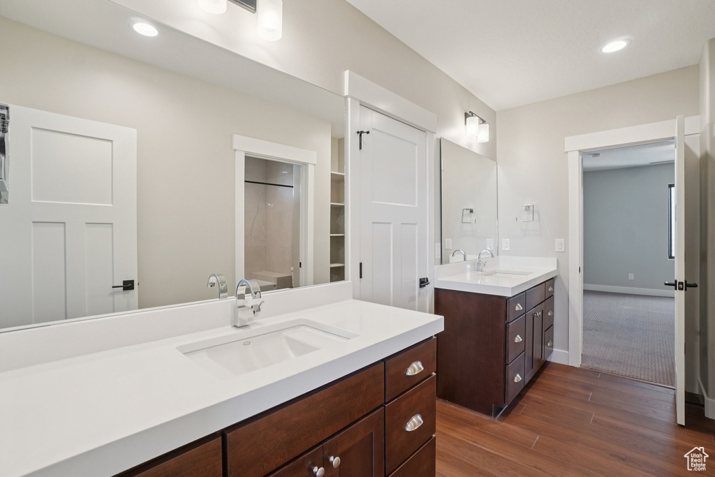 Bathroom featuring two vanities, wood finished floors, a shower, recessed lighting, and baseboards