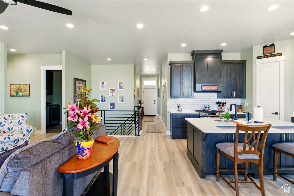 Kitchen with light countertops, a breakfast bar, light wood-type flooring, wall chimney exhaust hood, and recessed lighting