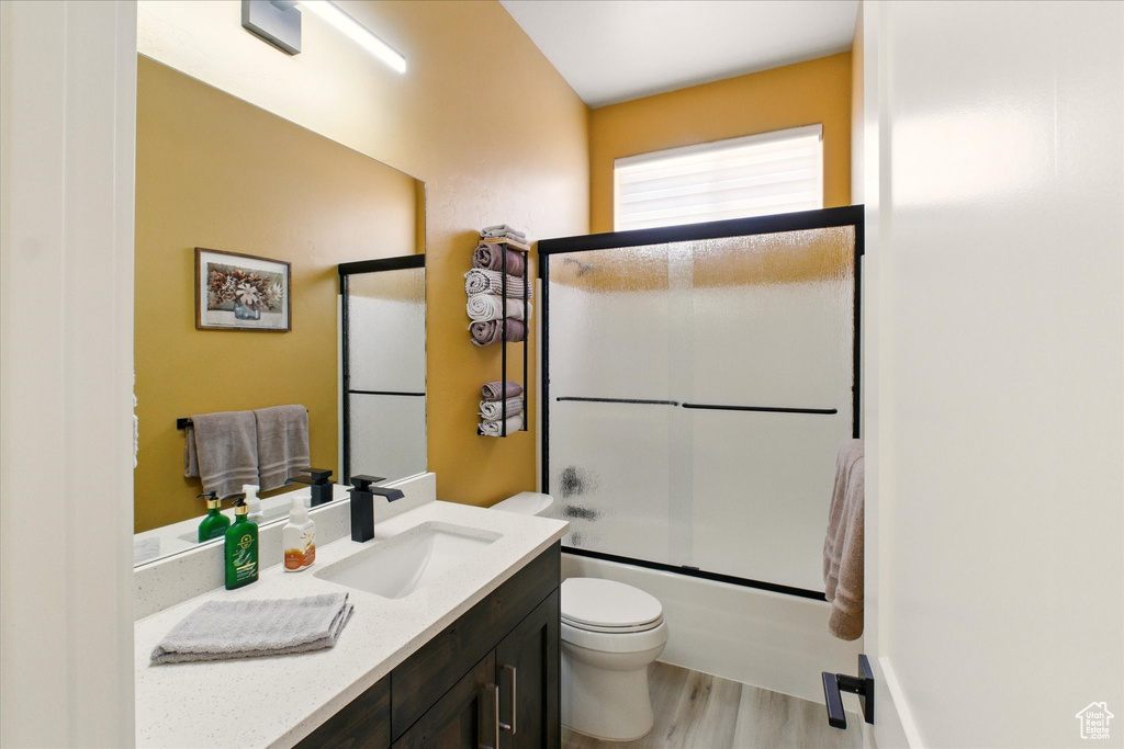 Bathroom with vanity, toilet, wood finished floors, and enclosed tub / shower combo