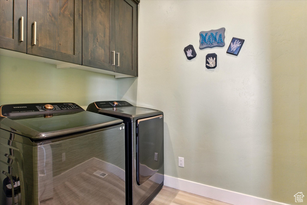 Laundry area featuring cabinet space, washing machine and dryer, baseboards, and light wood-style flooring
