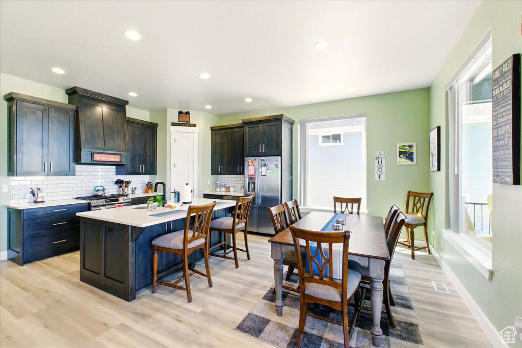 Kitchen featuring appliances with stainless steel finishes, a kitchen breakfast bar, light countertops, backsplash, and light wood-style floors