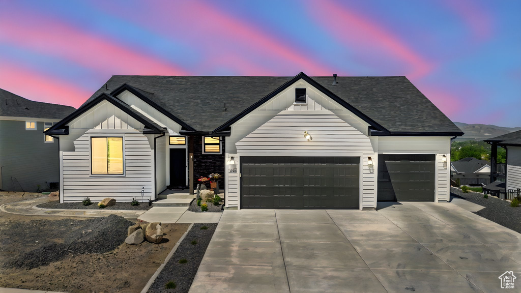 Modern farmhouse featuring a garage, board and batten siding, concrete driveway, and roof with shingles