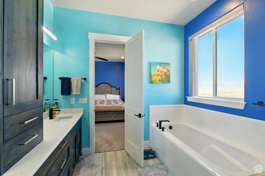 Ensuite bathroom featuring wood finished floors, vanity, a bath, and baseboards