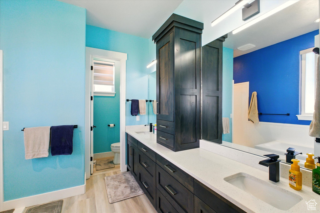 Bathroom with double vanity, toilet, plenty of natural light, and wood finished floors