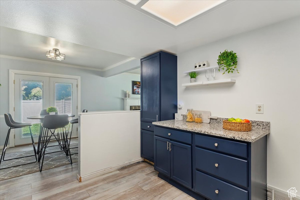 Kitchen with blue cabinetry, crown molding, light wood-style floors, light stone counters, and open shelves