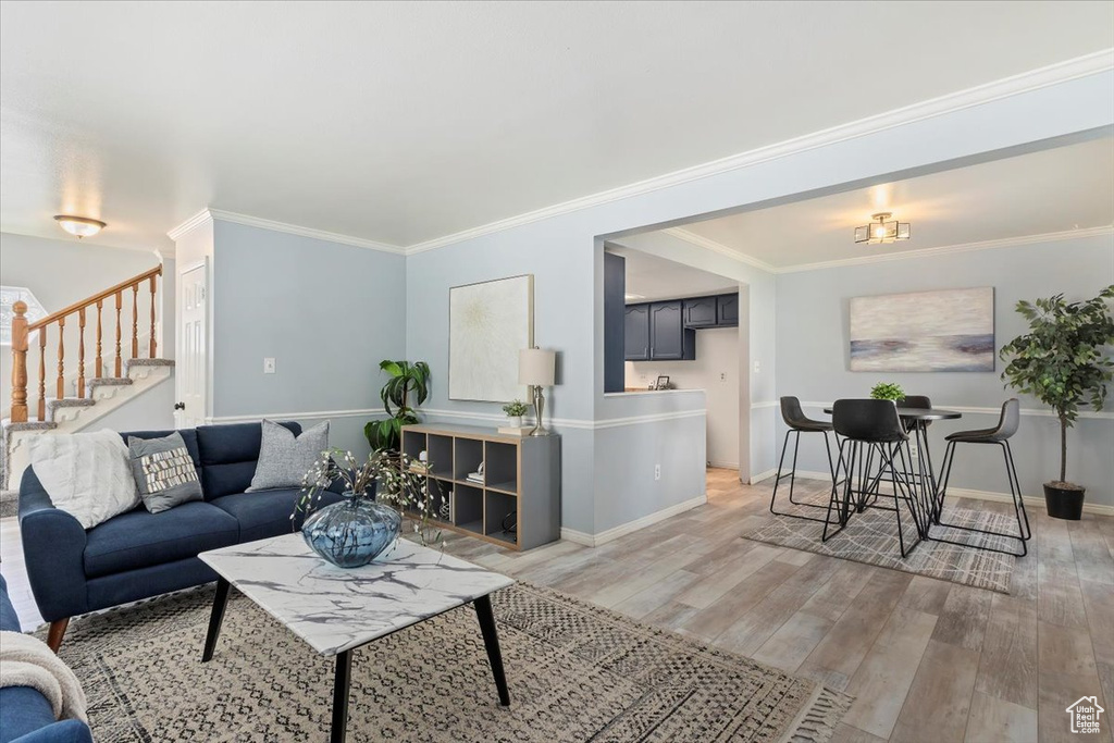 Living room featuring stairway, light wood-style flooring, baseboards, and crown molding