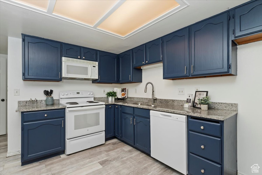 Kitchen with white appliances, a sink, blue cabinets, and light wood-style flooring