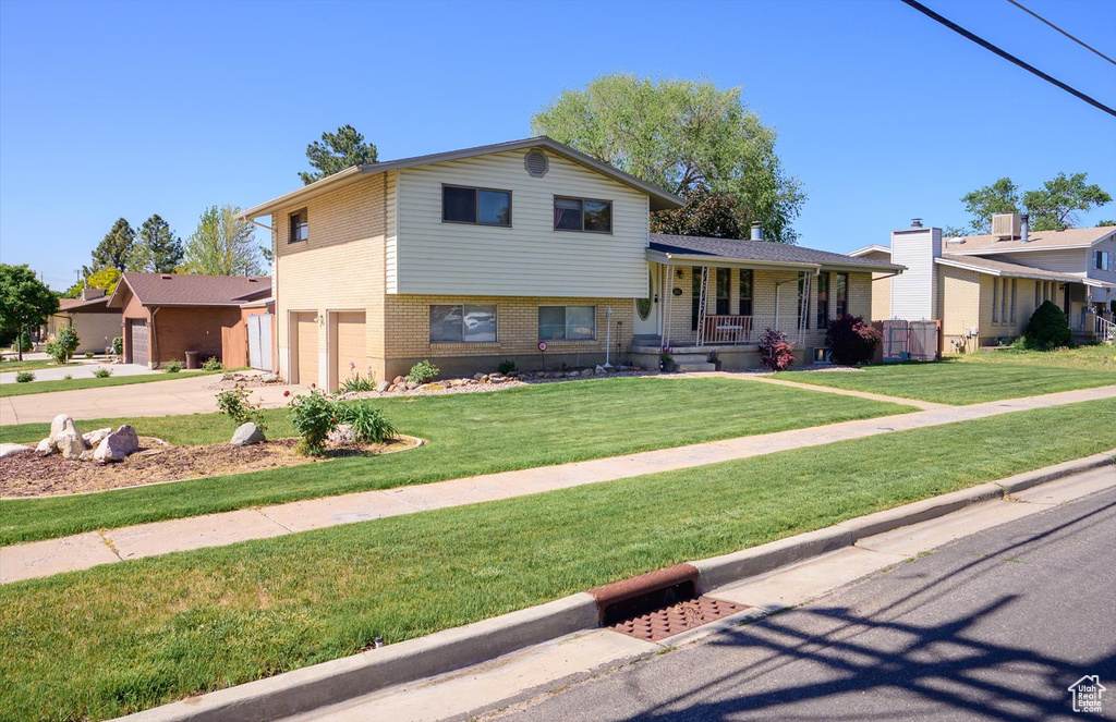 Split level home featuring brick siding, a porch, an attached garage, concrete driveway, and a front lawn