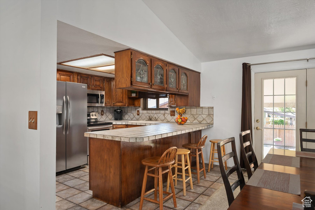 Kitchen featuring stainless steel appliances, decorative backsplash, a peninsula, lofted ceiling, and light countertops
