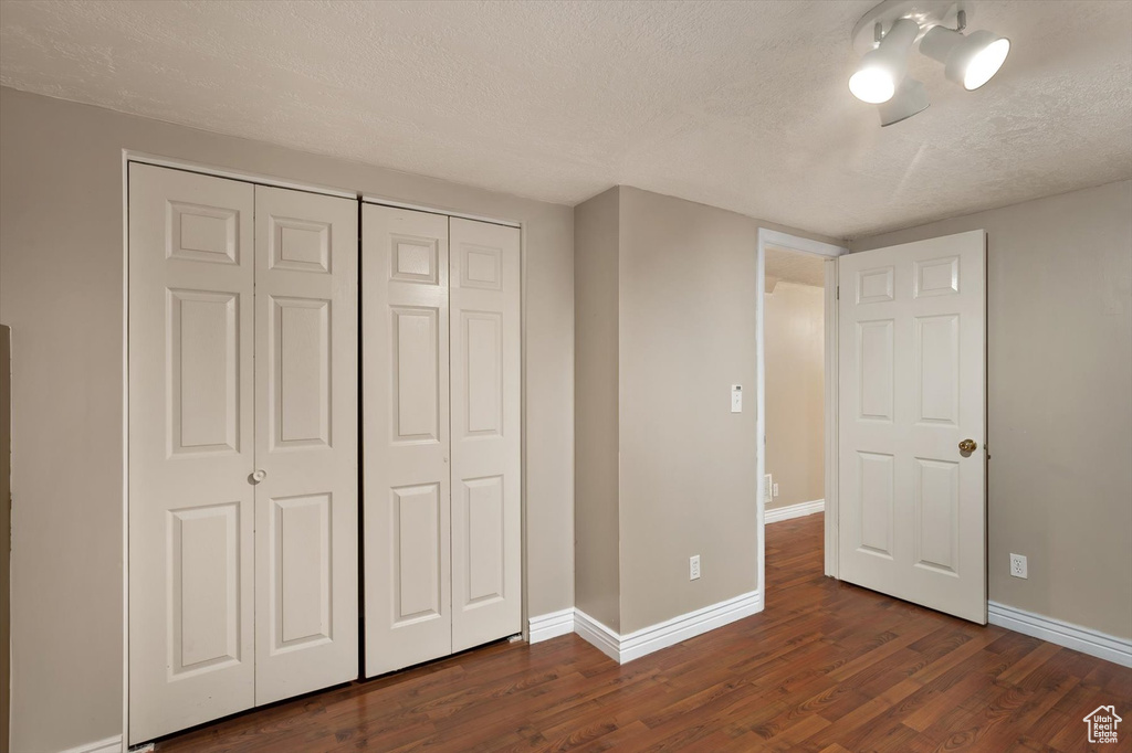 Unfurnished bedroom with a textured ceiling, dark wood finished floors, baseboards, and a closet