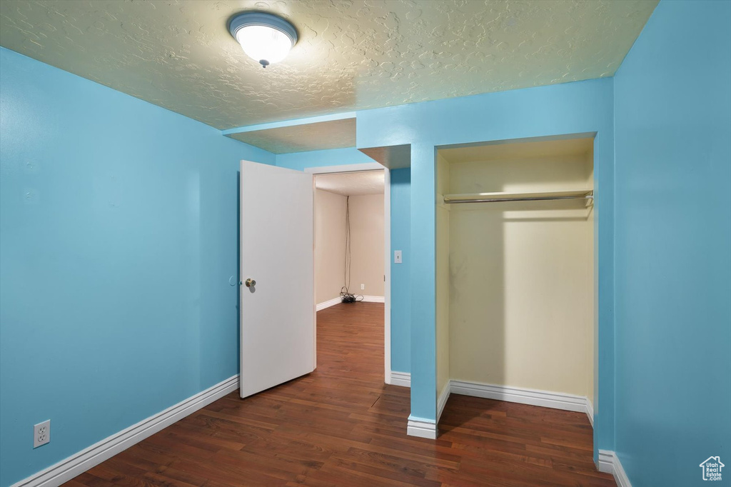 Unfurnished bedroom with a textured ceiling, wood finished floors, a closet, and baseboards