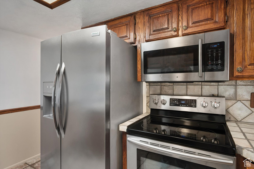 Kitchen with appliances with stainless steel finishes, brown cabinetry, backsplash, and light countertops