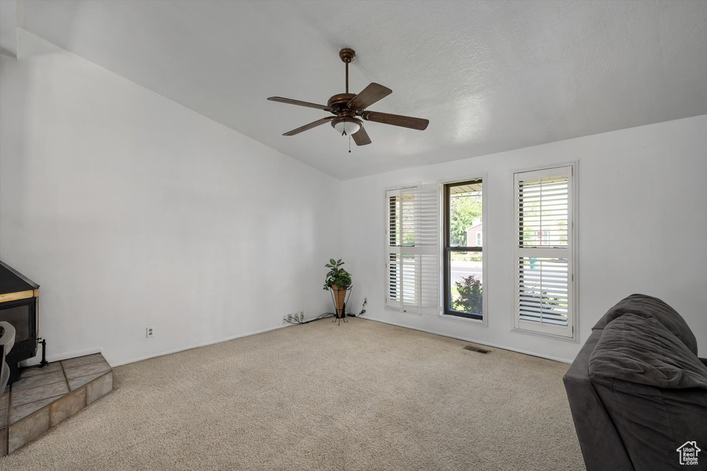 Carpeted living room with lofted ceiling, ceiling fan, and a wood stove