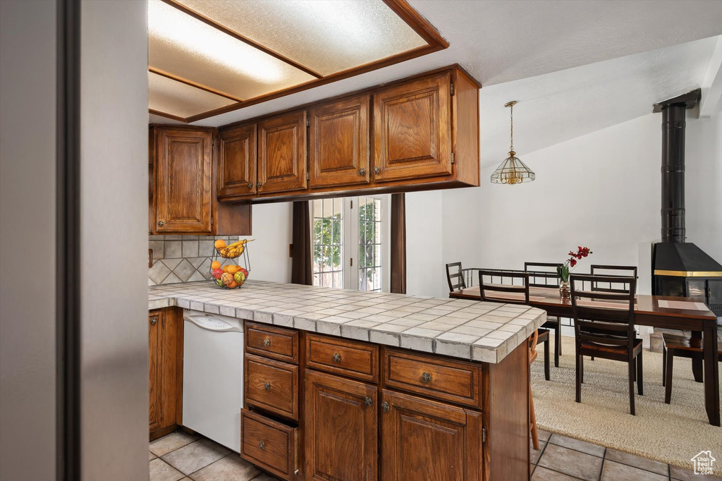 Kitchen with a peninsula, brown cabinetry, decorative backsplash, and light tile patterned flooring