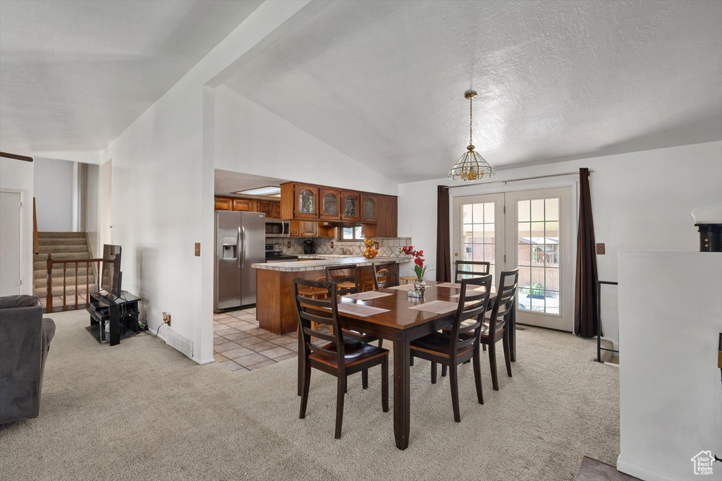 Dining space with light colored carpet, stairs, and lofted ceiling