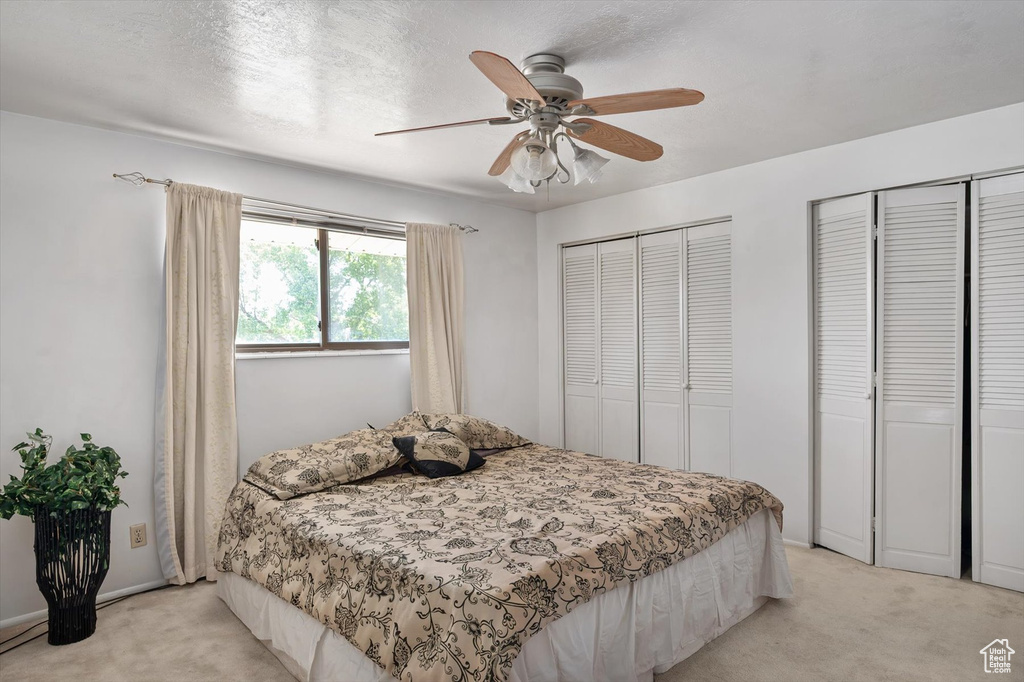 Bedroom with light colored carpet, two closets, and a ceiling fan