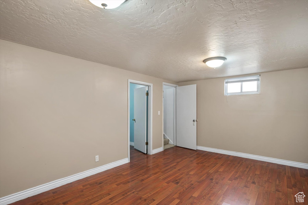 Empty room with a textured ceiling, wood finished floors, and baseboards