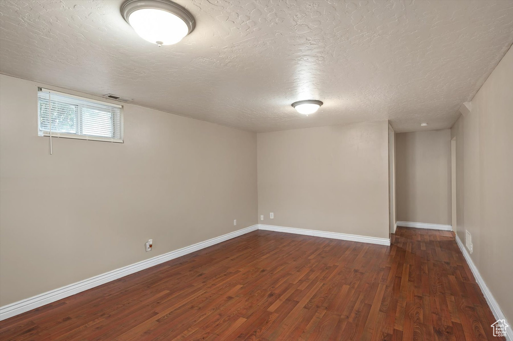 Basement featuring a textured ceiling, dark wood-style flooring, and baseboards