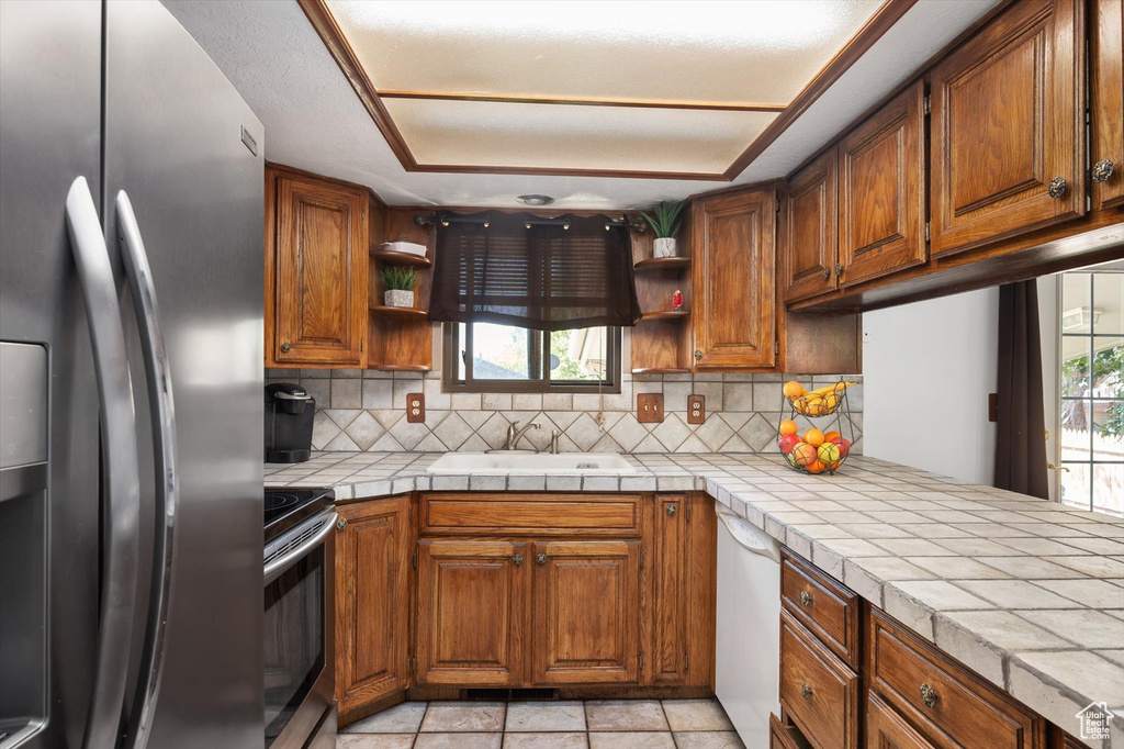 Kitchen with stainless steel appliances, open shelves, brown cabinets, and healthy amount of natural light