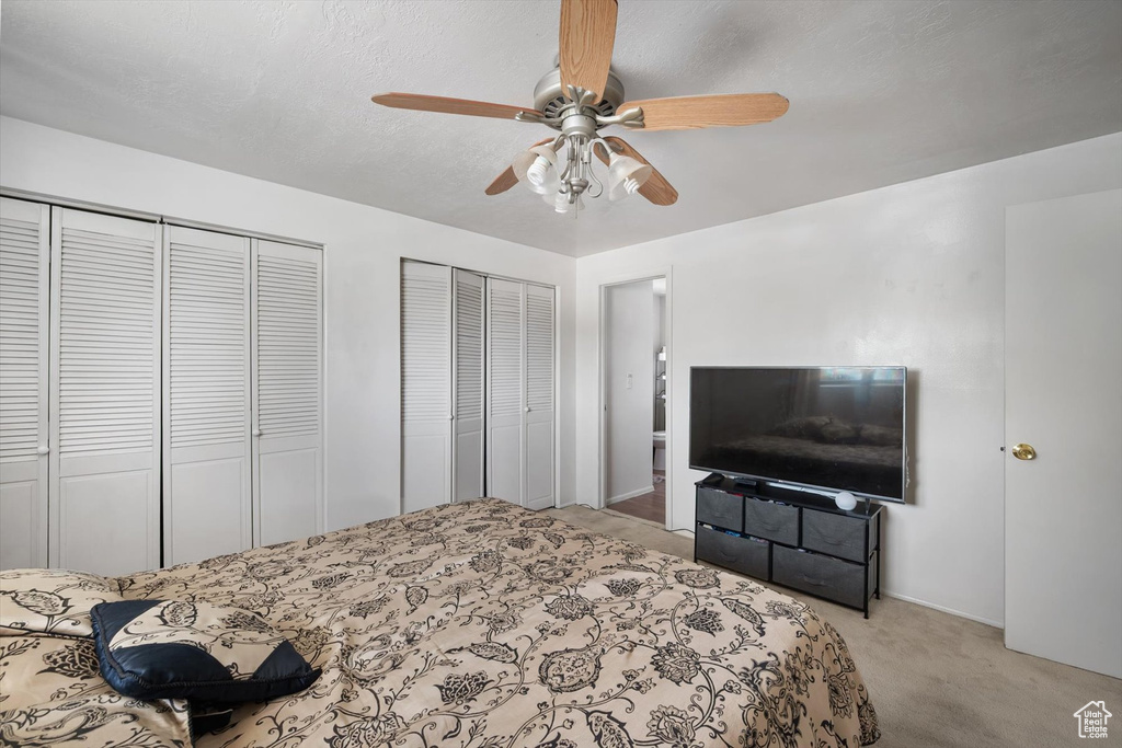 Bedroom with two closets, carpet, and a ceiling fan