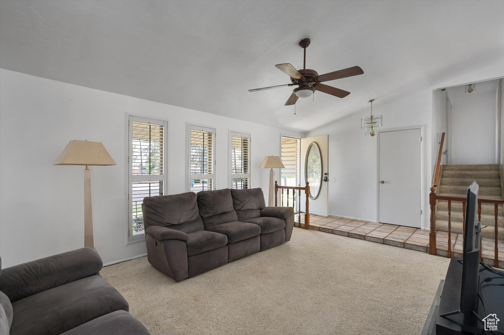 Carpeted living room with a ceiling fan, plenty of natural light, vaulted ceiling, stairway, and baseboards