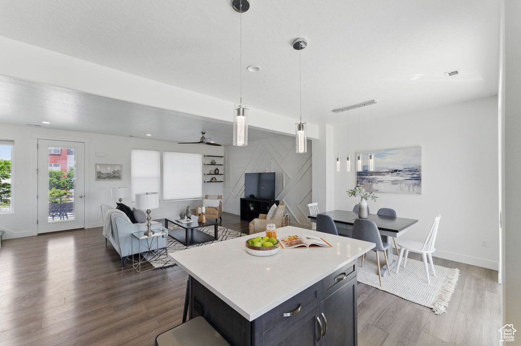 Kitchen featuring dark wood-type flooring, light countertops, decorative light fixtures, a center island, and baseboards