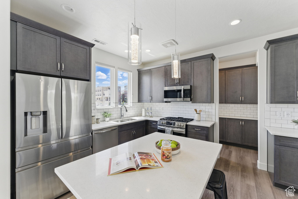 Kitchen featuring appliances with stainless steel finishes, a sink, light countertops, backsplash, and dark wood-style floors