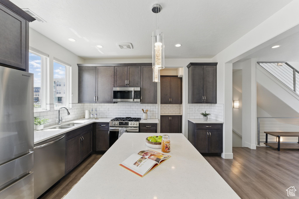 Kitchen featuring appliances with stainless steel finishes, a sink, dark wood-type flooring, light countertops, and dark brown cabinetry