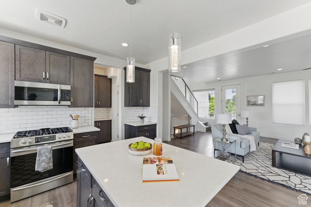 Kitchen featuring stainless steel appliances, light countertops, wood finished floors, dark brown cabinetry, and decorative backsplash