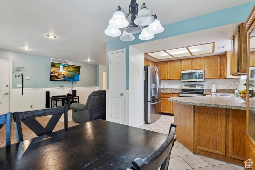 Kitchen with stainless steel appliances, light tile patterned floors, a chandelier, brown cabinets, and a peninsula