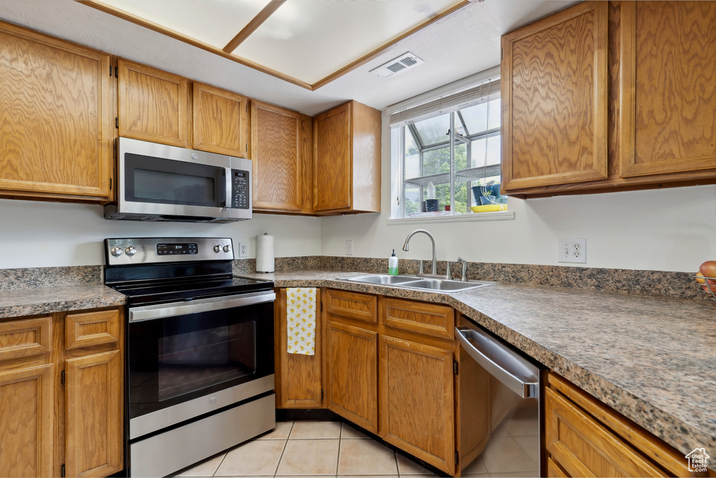 Kitchen with appliances with stainless steel finishes, a sink, light tile patterned floors, and brown cabinetry