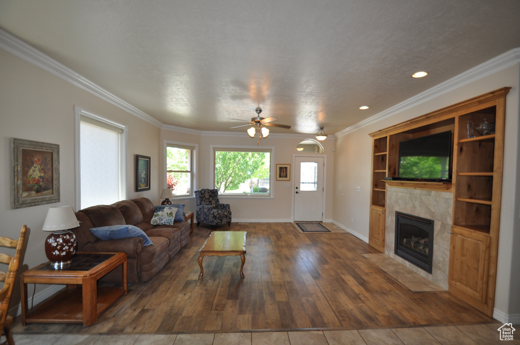 Living area with a premium fireplace, a ceiling fan, ornamental molding, wood finished floors, and baseboards