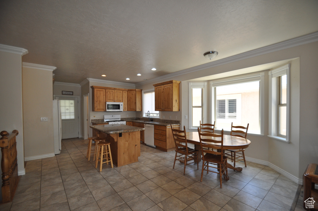 Kitchen with white appliances, ornamental molding, a center island, baseboards, and a sink