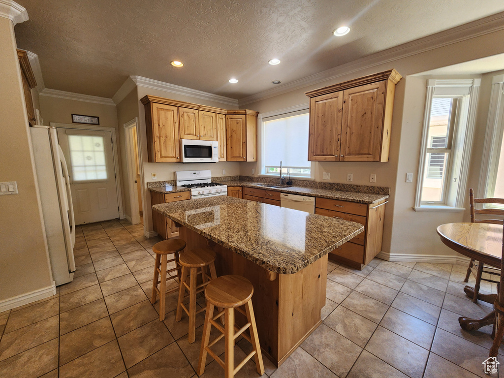 Kitchen with white appliances, a sink, baseboards, a breakfast bar, and a kitchen island
