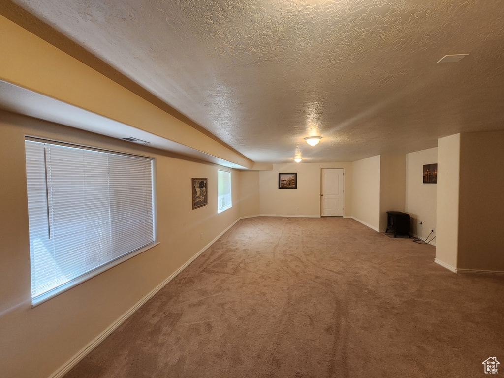 Basement with a textured ceiling, carpet flooring, baseboards, and a wood stove