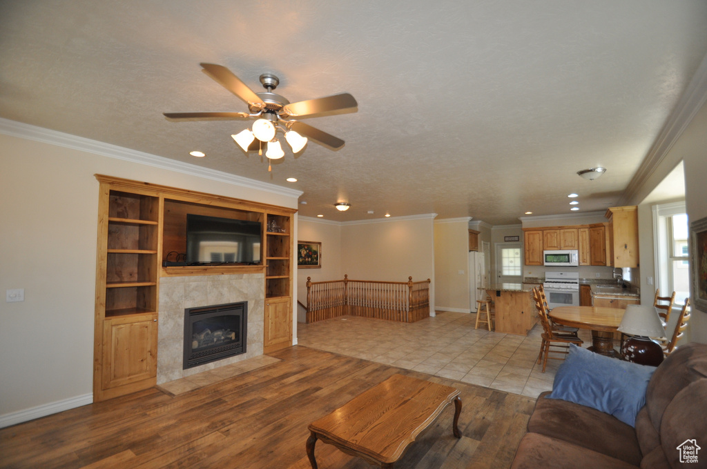 Living room featuring light wood-type flooring, a ceiling fan, recessed lighting, baseboards, and crown molding