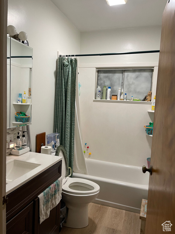 Bathroom with wood finished floors, vanity, shower / bath combination with curtain, and toilet