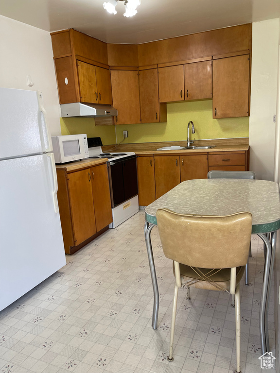 Kitchen with white appliances, a sink, under cabinet range hood, light flooring, and brown cabinetry