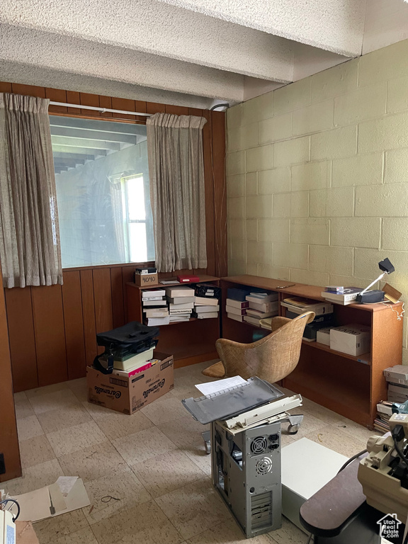 Office space with concrete block wall, tile patterned floors, wooden walls, and a textured ceiling