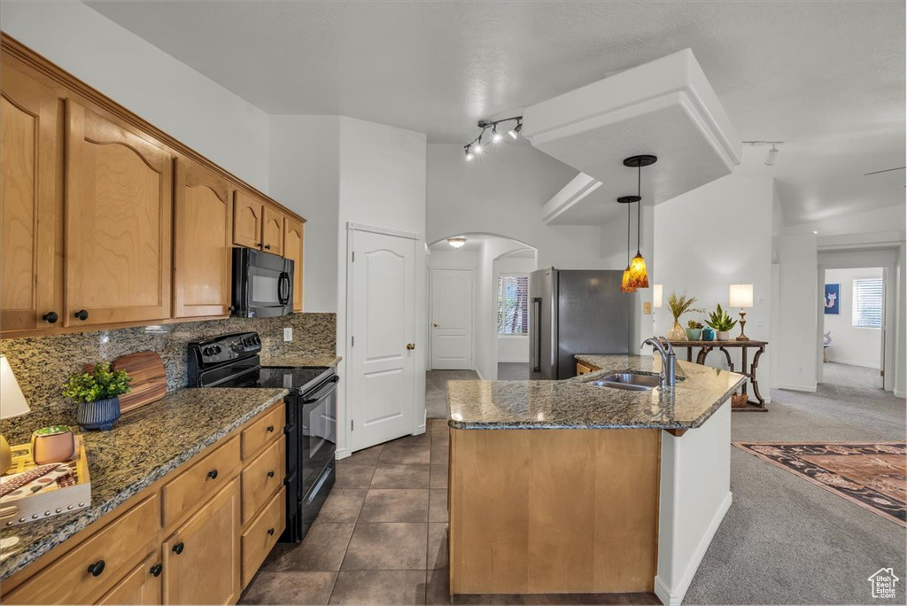 Kitchen with black appliances, a sink, arched walkways, backsplash, and dark stone counters
