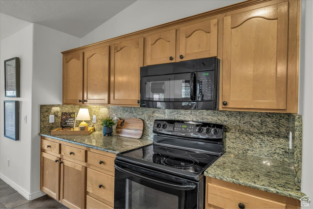 Kitchen featuring black appliances, backsplash, stone countertops, vaulted ceiling, and baseboards