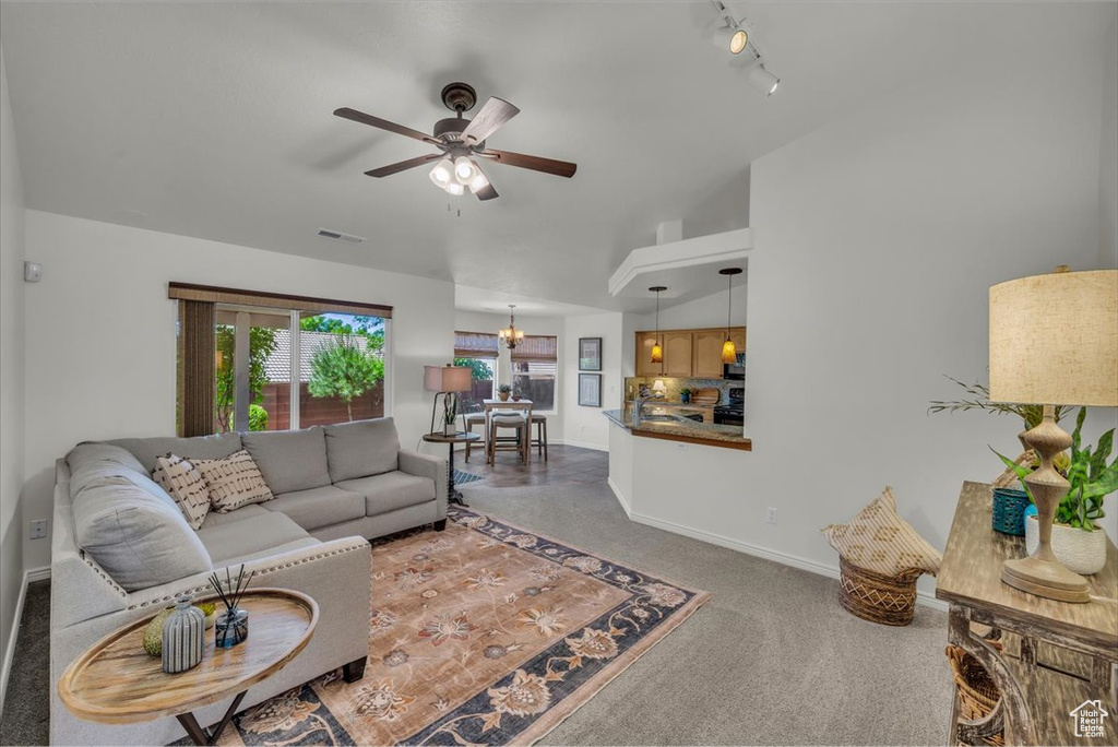 Living room featuring carpet floors, a ceiling fan, rail lighting, a chandelier, and baseboards