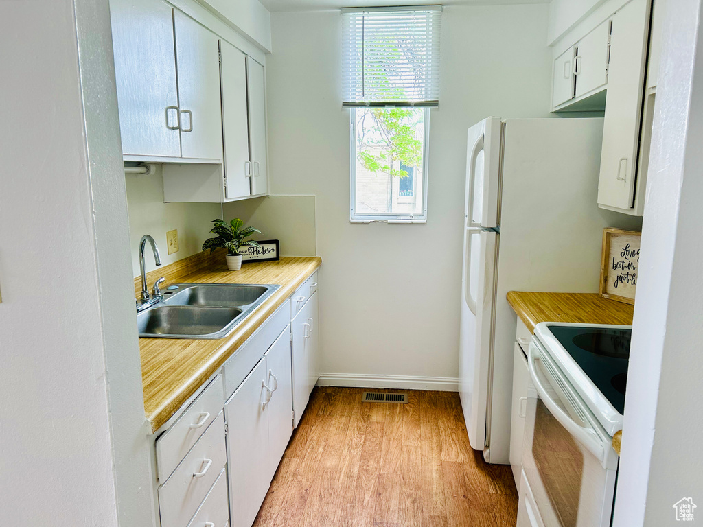 Kitchen with white range with electric stovetop, a sink, light wood finished floors, light countertops, and baseboards