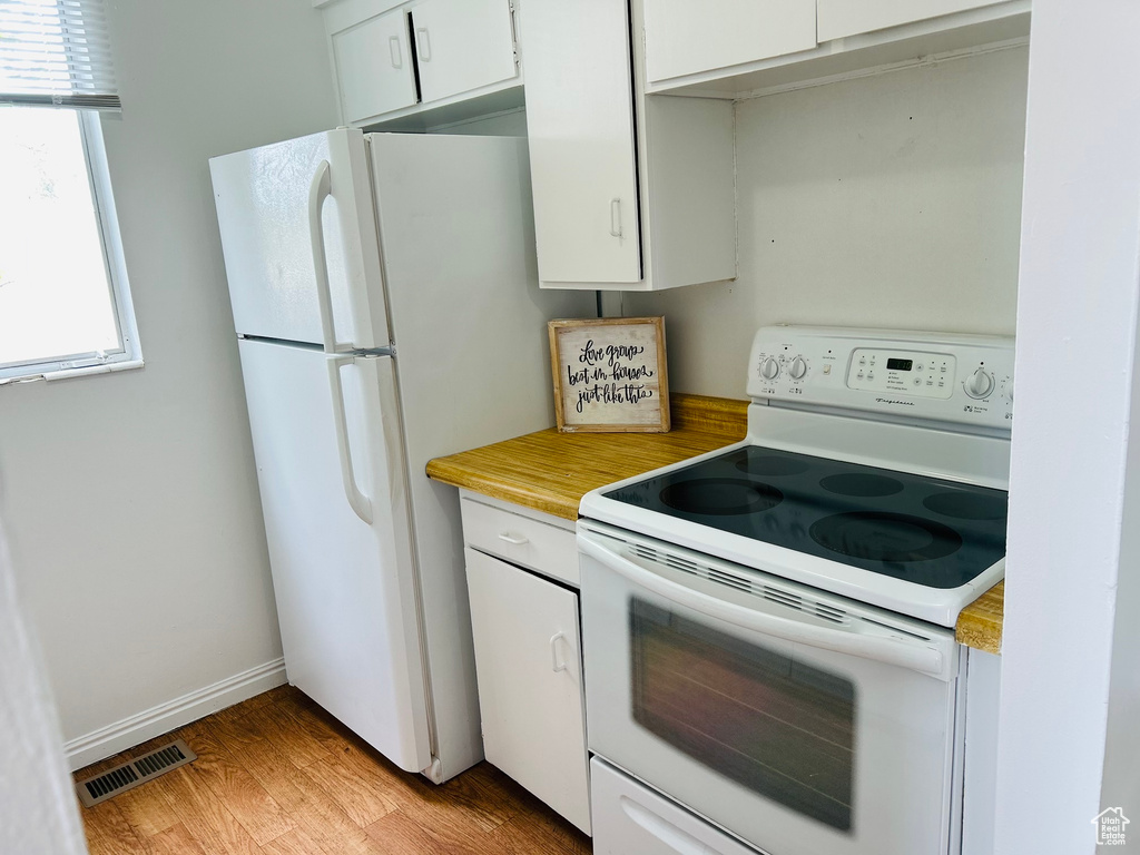 Kitchen with white appliances, white cabinetry, light wood-type flooring, and light countertops